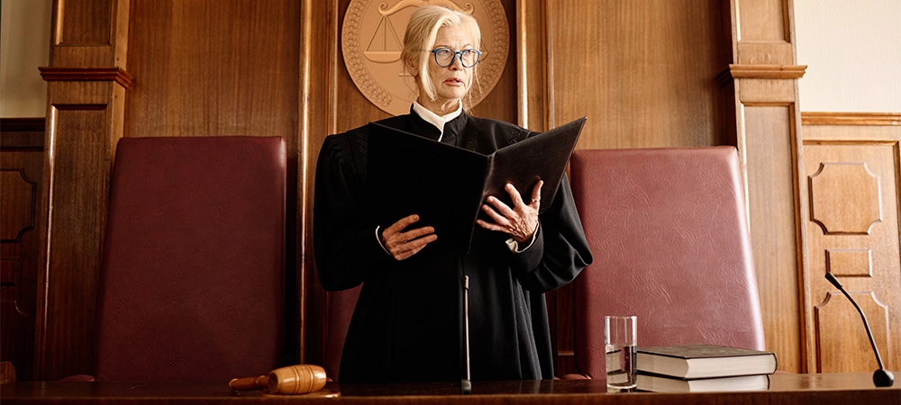 Confident mature blond female judge with open folder standing by desk